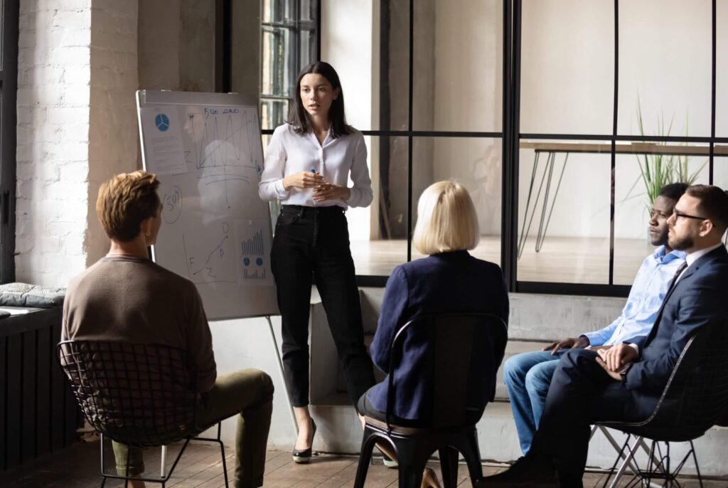 Confident lady business trainer coach leader give flip chart presentation consulting clients teaching employees training team people speaking explaining strategy at marketing workshop concept