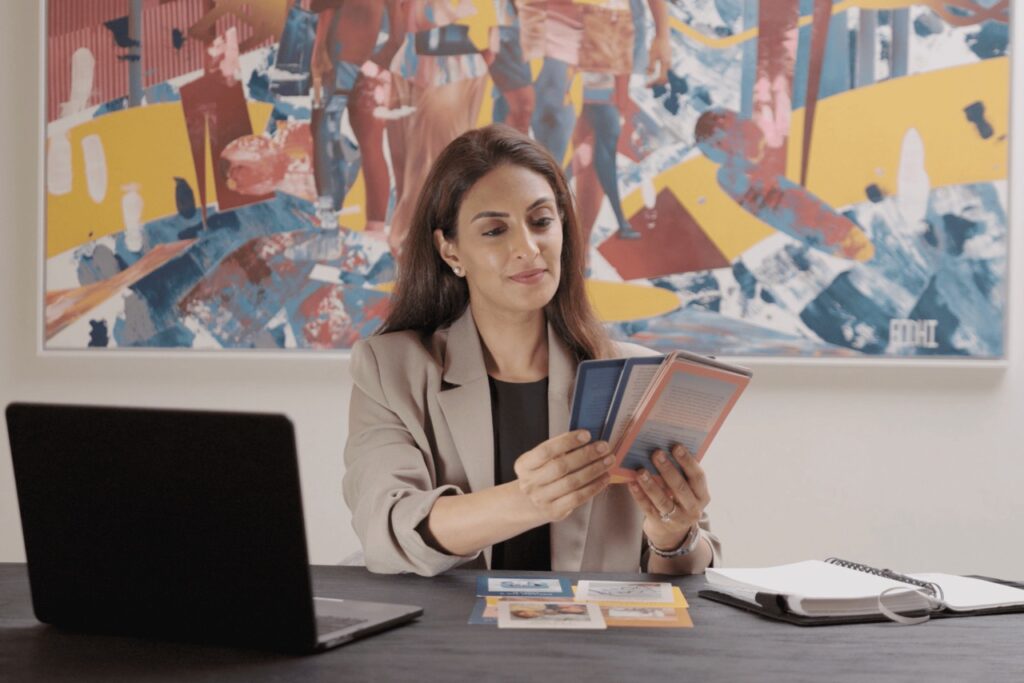 Shireena holding up Getting To Happy cards while sitting on a work table with her laptop and journal out